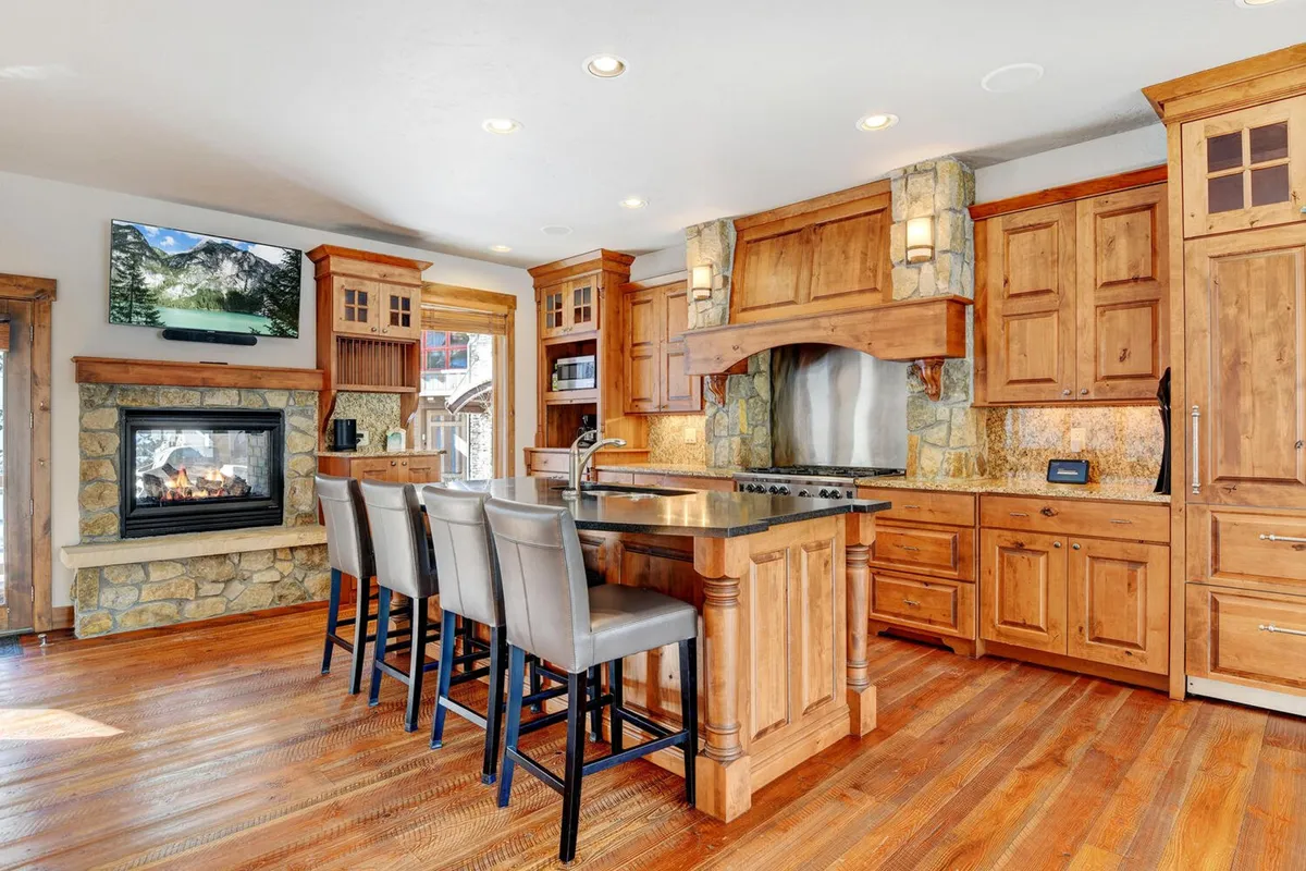 A kitchen scene with a central island, cabinetry, and a visible fireplace, plus a television in the background. The mood is lively and welcoming, suggesting a space designed for cooking, entertaining, and gathering. The setup hints at celebrations, casual brunches, and memorable family moments.