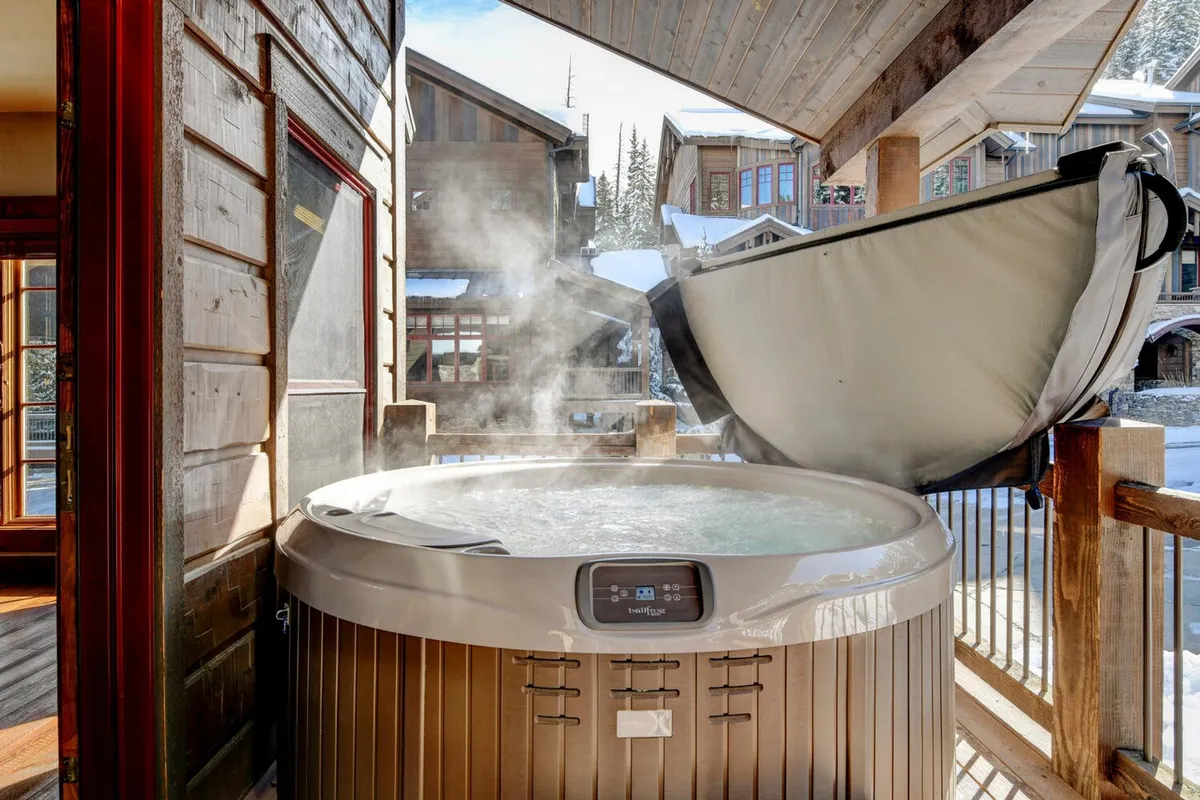 An inviting outdoor scene featuring a steaming hot tub surrounded by beautiful architecture. With snow on the ground and steam rising, the image evokes the soothing relaxation that awaits after a day of snowy adventures.