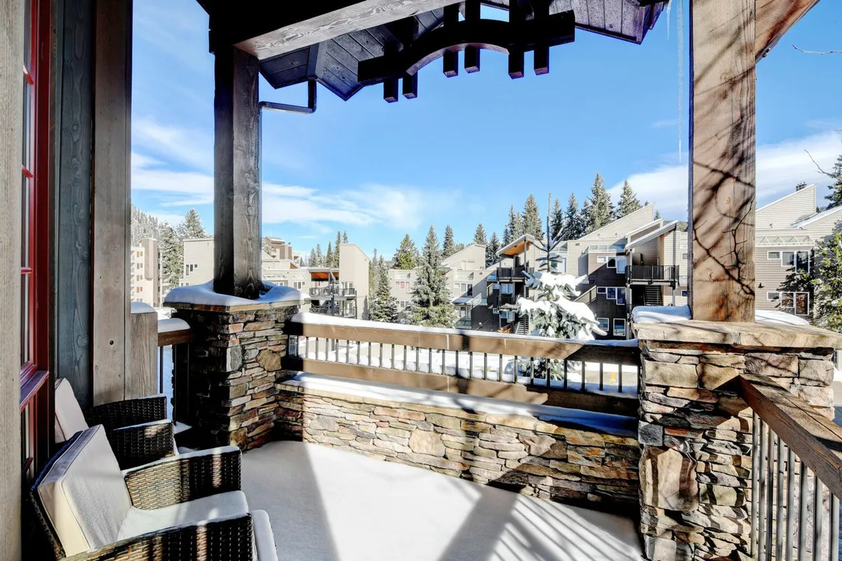 A cozy exterior seating area with a stone railing and wooden beams, overlooking breathtaking mountain vistas. The setting is perfect for relaxing with a coffee, reading, or socializing while enjoying the natural beauty.