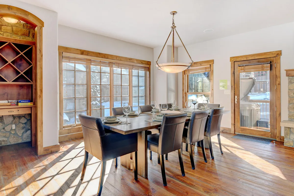 A spacious dining area is shown, with a large dining table set beneath a chandelier and expansive windows letting in natural light. Wine storage and elegant décor add to the inviting atmosphere, making it ideal for shared meals and celebrations.