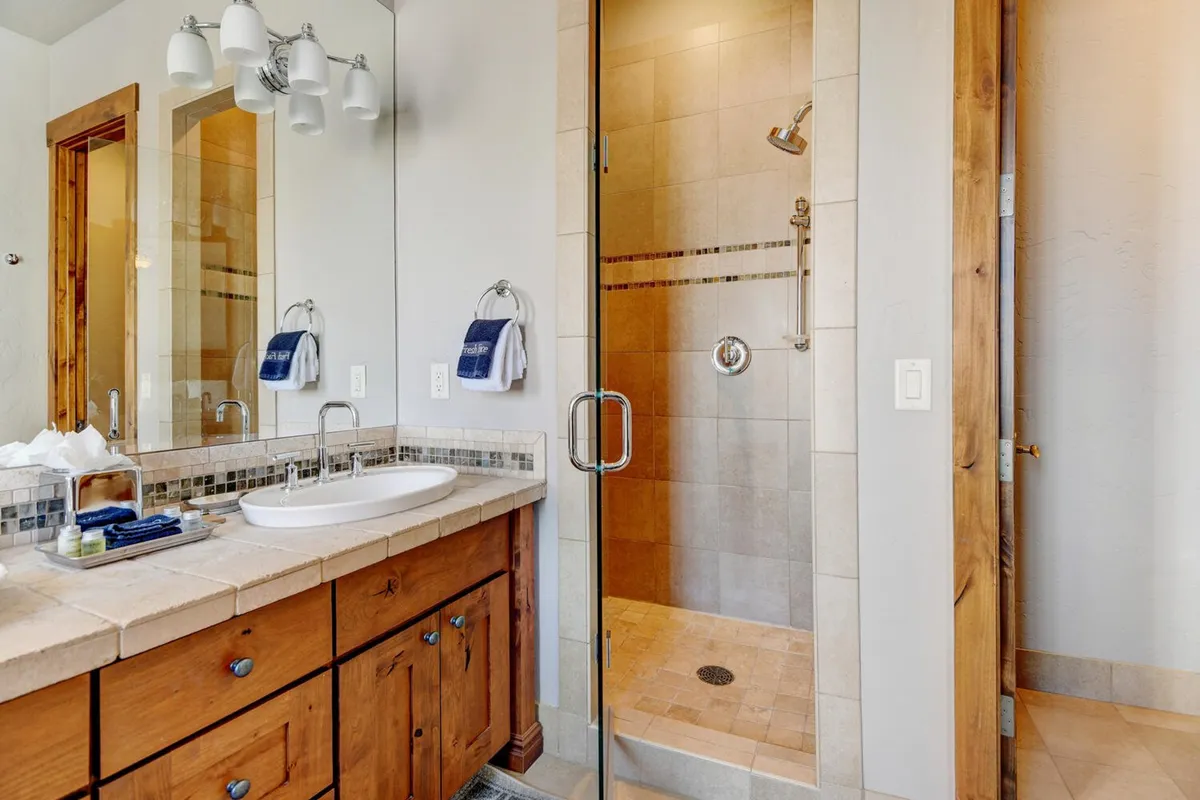 A modern, spa-inspired bathroom boasting a vanity with a sink, glass shower enclosure, and rich wooden cabinetry. Soft lighting and thoughtful amenities evoke a sense of tranquility and luxurious self-care.