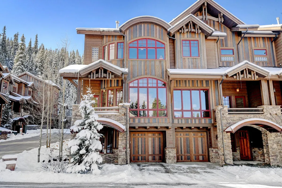 The hero image showcases a stunning luxury mountain villa with a striking wooden facade, large arched windows, and beautiful stone accents, all surrounded by a pristine, snow-covered landscape and towering pine trees. The villa sits against a backdrop of majestic, snow-capped mountains, evoking both adventure and relaxation.