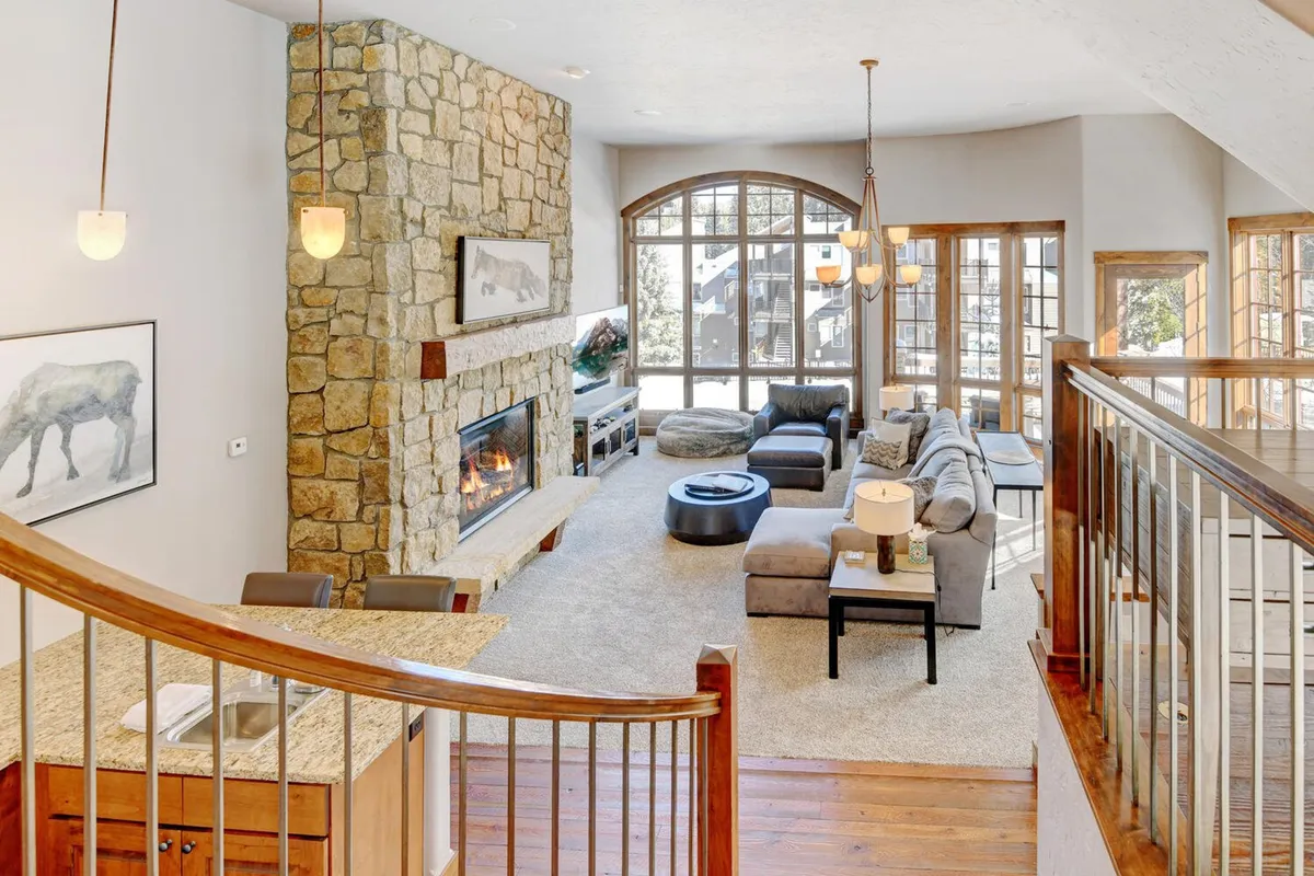 A welcoming living area featuring a large stone fireplace, big windows that invite in the scenery, and a comfortable seating arrangement. The ambiance is warm and perfect for gathering or relaxing after outdoor activities.